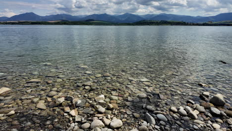 Clear-lake-with-rocky-shoreline-and-mountain-backdrop