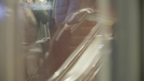 Blurred-view-of-people-walking-on-an-escalator-through-a-reflective-glass