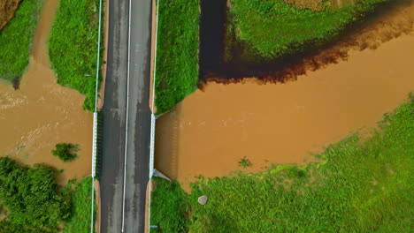 Top-down-drone-shot-of-a-bridge,-brown-water-in-a-flooding-river-and-farmlands