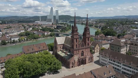 Vídeo-De-Dron-En-4K-De-Una-Iglesia-Histórica-En-Basilea,-Suiza,-Con-Edificios-Modernos-A-Lo-Lejos-Al-Otro-Lado-Del-Río-Rin