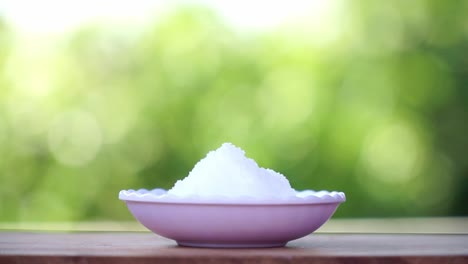 A-small-bowl-full-of-white-crystal-salt-with-green-blur-nature-background