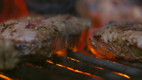 Delicious-Sirloin-Steaks-Being-Flame-Grilled-on-BBQ-with-Fire-in-Background-and-Chef-Moving-Meat-on-Grill-in-Slow-Motion-4K