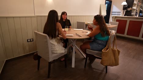 Una-Mujer-Habla-Con-Dos-Amigas-En-Un-Acogedor-Ambiente-De-Restaurante.