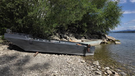 Barcos-Viejos-En-La-Orilla-Rocosa-Del-Lago-Bajo-Un-árbol