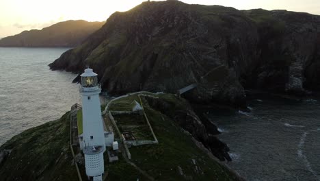 Luftaufnahme-Des-Leuchtturms-South-Stack,-Vorbei-An-Einem-Nautischen-Wahrzeichen-Der-Insel-Während-Des-Sonnenaufgangs-Zur-Goldenen-Stunde