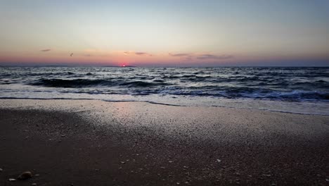 Waves-gently-lap-at-the-shore-as-the-sun-sets-over-the-Sea-of-Azov,-creating-a-stunning-display-of-colors-in-the-sky