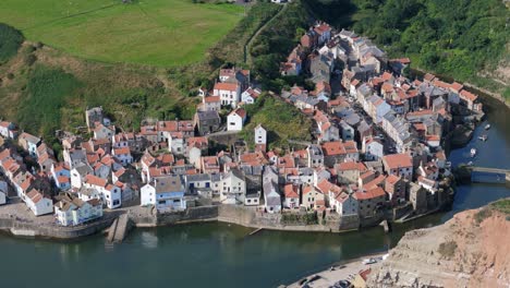 Aerial-drone-view-of-Staithes-Harbour-on-the-North-Yorkshire-coast-with-river,houses,-boats-on-a-sunny-morning-in-August,-summertime