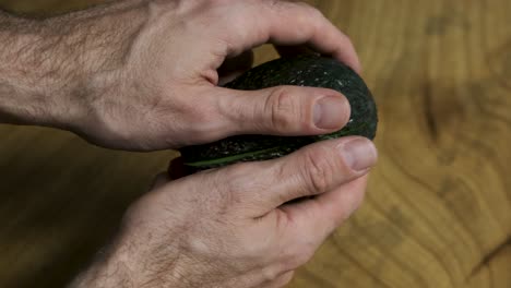 A-young-man-opening-an-avocado-in-half-on-wooden-table-background