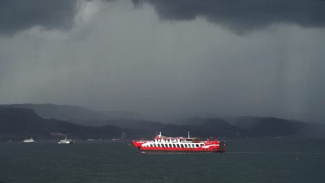 A-passenger-ferry-sails-toward-island-in-front-of-a-dark-rain-storm,-Slow-motion,-East-Java-Indonesia