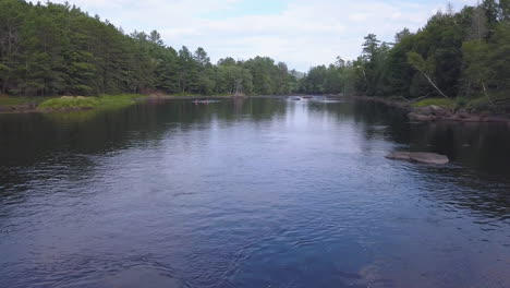 Cinematic-drone-shot-flying-low-over-a-calm-river,-canoes-paddling-down-the-Madawaska-River