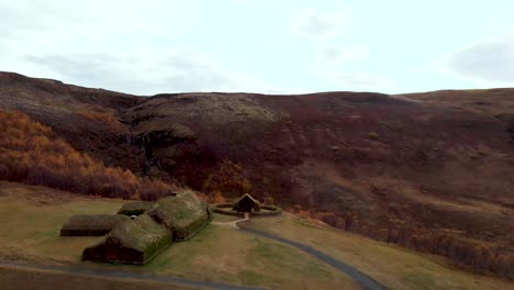 Aerial-4k-view-of-a-couple-sitting-near-traditional-Icelandic-Turf-Houses-in-autumn-with-a-beautiful-landscape,-Iceland,-Europe,-reveal-shot