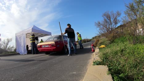 Equipo-De-Boxes-Masculino-Sentado-En-La-Cuneta-Junto-A-La-Carretera-En-La-Colina-En-Imtahleb,-Malta,-Esperando-Que-Los-Autos-Sean-Revisados-En-La-Parada-De-Boxes---GoPro-Timelapse