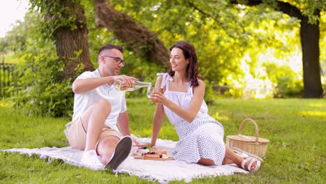 Glückliches-Paar-Trinkt-Wein-Im-Sommerpark.Freizeit--Und-Personenkonzept.-Glückliches-Paar-Stößt-Mit-Getränken-An-Und-Macht-Picknick-Im-Sommerpark