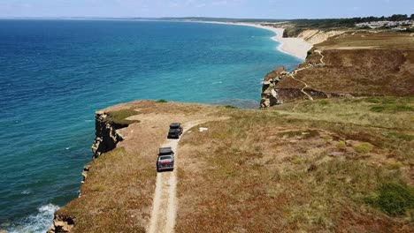 Aerial-view-Classic-cars-drive-along-a-seaside-cliff-in-Portugal