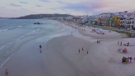 Toma-Aérea-De-Una-Plataforma-Rodante-Sobrevolando-La-Playa-De-Bombas-Con-Turistas-Justo-Después-Del-Atardecer-En-Brasil