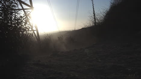 Mountain-biker-riding-down-rocky-face-under-power-lines-at-sunset-and-panning-camera