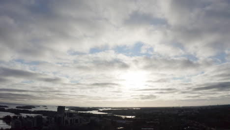 Tilt-down-arial-view-of-coastal-city-and-sunset-behind-the-clouds