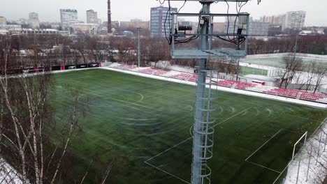 Drone-moving-up-following-an-electric-light-beside-a-soccer-training-pitch-in-snowy-Moscow,-Russia