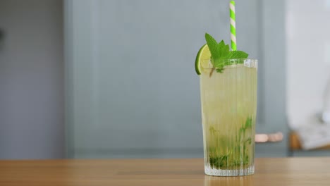 Hand-Nimmt-Ein-Glas-Mojito-Cocktail-Vom-Tisch.-Getränkekonzept-Hand-Einer-Frau-Nimmt-Ein-Glas-Limetten-Mojito-Cocktail-Vom-Tisch-Zu-Hause