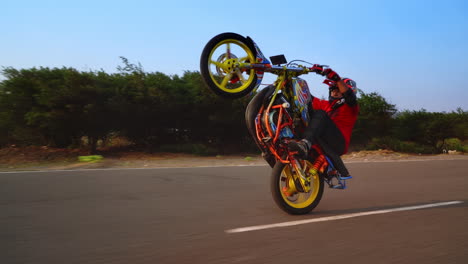 Tracking-shot-following-a-stunt-rider-closely-as-he-drives-down-the-road-on-his-back-wheel,-also-known-as-a-wheelie