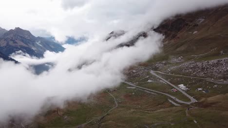 Clouds-hang-low-on-a-hillside-with-winding-road-in-rocky-mountain-landscape