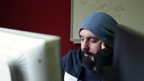 Creative-young-man-with-hat-and-gloves-thinking-in-front-of-monitors-in-his-studio,-focused-on-his-professional-work,-concept-design