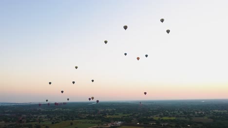 Globos-Aerostáticos-Volando-En-El-Cielo-Púrpura-De-Myanmar,-Sobre-El-Hermoso-Paisaje---Toma-Aérea