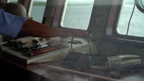 Close-up-shot-of-an-Indonesian-captain's-hand-adjusting-the-speed-levers-of-his-ship,-Slow-Motion-through-window-view