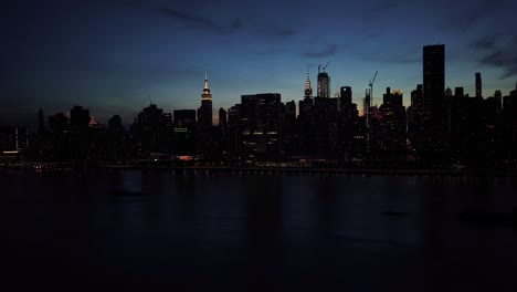 Motion-Time-Lapse-of-the-Manhattan-skyline-at-sunset,-the-sun-slowly-setting-behind-the-skyscrapers,-boats-floating-on-East-River,-June-2019