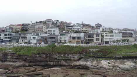 Aerial:-Drone-tracking-right-along-the-cliffs-over-the-beach-on-an-overcast-cloudy-day,-near-Bondi-Sydney