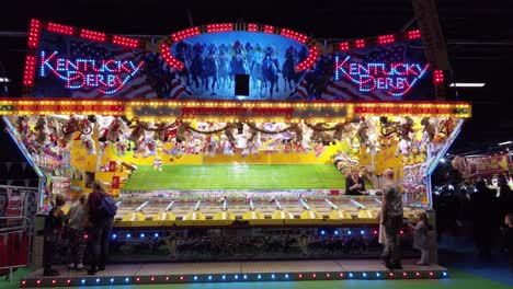 Tracking-shot-of-Kentucky-Derby-stall-game-at-funfair-lots-of-coloured-flashing-lights-and-signage