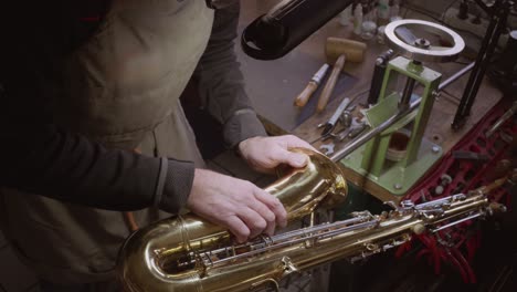 Skilled-Instrument-maker-repairing-dents-in-golden-saxophone-bell-and-body-by-hand