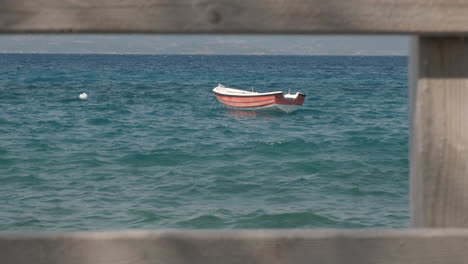 Still-shot-of-a-moored-boat-in-the-greek-coast-framed-with-a-wooden-balaustrade