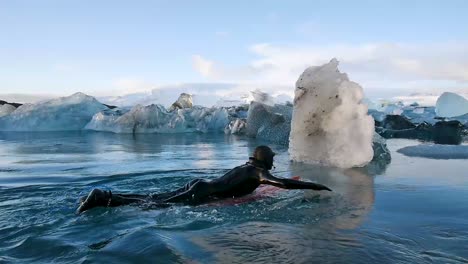 Surfer-paddling-through-icebergs-in-frozen-river-in-Iceland