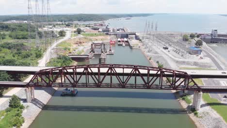 Railroad-and-vehicular-bridge-above-water-with-barges-docked-at-port-in-background,-Kentucky,-backward-aerial