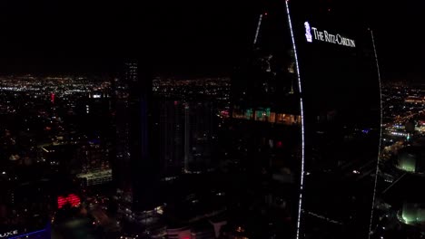 Aerial-descending-shot-of-a-reflective-glass-hotel-skyscraper-at-night