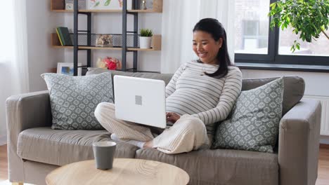 Feliz-Mujer-Asiática-Embarazada-Con-Computadora-Portátil-En-Casa.-Concepto-De-Embarazo,-Descanso,-Personas-Y-Expectativas-Feliz-Sonriente-Mujer-Asiática-Embarazada-Con-Computadora-Portátil-Sentada-En-Un-Sofá-En-Casa