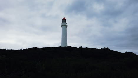 Lone-lighthouse-standing-on-dark-rocky-hill-with-soft-cloudy-background,-static