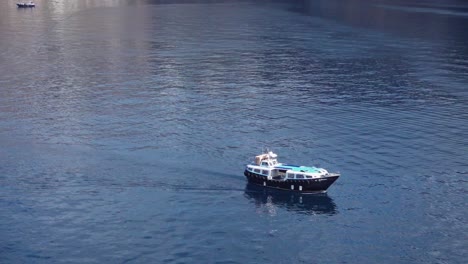 Vista-Lateral-Del-Ferry-En-Barco-Tierno-En-Aguas-Tranquilas-Con-Reflejos-De-La-Isla-Mediterránea-En-La-Caldera-De-Santorini-En-Grecia