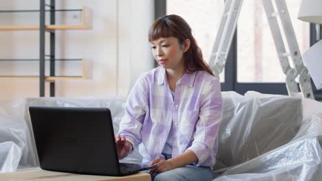 Mujer-Con-Computadora-Portátil-Mudándose-A-Una-Nueva-Casa.-Mudanza,-Personas-Y-Concepto-De-Bienes-Raíces.-Mujer-Asiática-Feliz-Y-Sonriente-Con-Computadora-Portátil-Y-Cajas-En-Una-Nueva-Casa