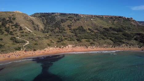 Toma-Aérea-De-Un-Dron-Volando-Hacia-Atrás-Desde-Una-Hermosa-Playa-En-Malta-En-Un-Día-Brillante-Y-Soleado