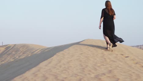 Woman-dressed-in-black-is-walking-on-the-dunes-in-the-desert-of-Dubai-Emirates