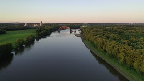 Arched-Bridge-and-Wide-River-in-Green-Landscape,-Long-shot,-Aerial-Forward-Dolly