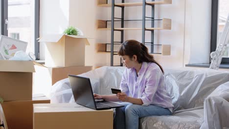 Woman-with-Laptop-and-Credit-Card-at-New-Home.moving,-people-and-real-estate-concept--happy-smiling-asian-woman-with-laptop-computer-and-credit-card-at-new-home