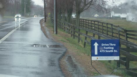 4k:-Straßenaufnahme-An-Einem-Regnerischen-Tag-Mit-Verkehr-Vor-Einem-Schild-Mit-Der-Aufschrift-„Drive-Thru-Test“-Für-Den-Coronavirus-Ausbruch