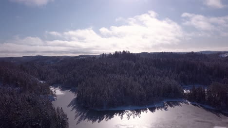 Vista-Aérea-Tomada-Con-Un-Dron-Sobre-Un-Lago-Helado,-Colinas-Y-Bosques-En-Un-Día-Soleado-De-Invierno-En-Risvann,-Birkeland,-Agder,-Sur-De-Noruega