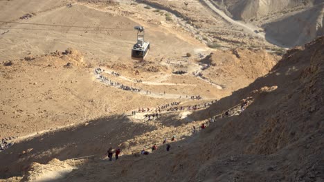 Masada-cableway-cable-car-with-tourists-hiking-iconic-snake-path-below,-Israel