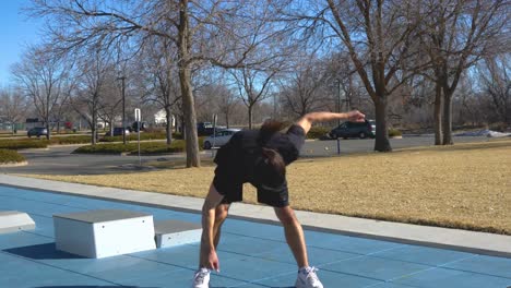 Long-haired,-Bearded-man-does-windmill-exercise-at-park-on-sunny-day