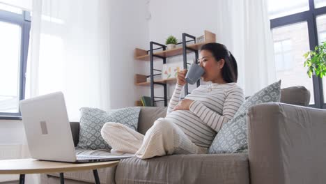 Feliz-Mujer-Asiática-Embarazada-Con-Computadora-Portátil-En-Casa.-Concepto-De-Embarazo,-Descanso,-Personas-Y-Expectativas-Feliz-Sonriente-Mujer-Asiática-Embarazada-Con-Computadora-Portátil-Sentada-En-Un-Sofá-En-Casa