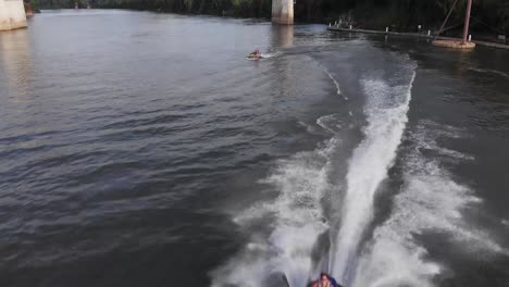 Two-personal-watercrafts-in-dark-river-water-and-rider-approaches-camera,-overhead-aerial